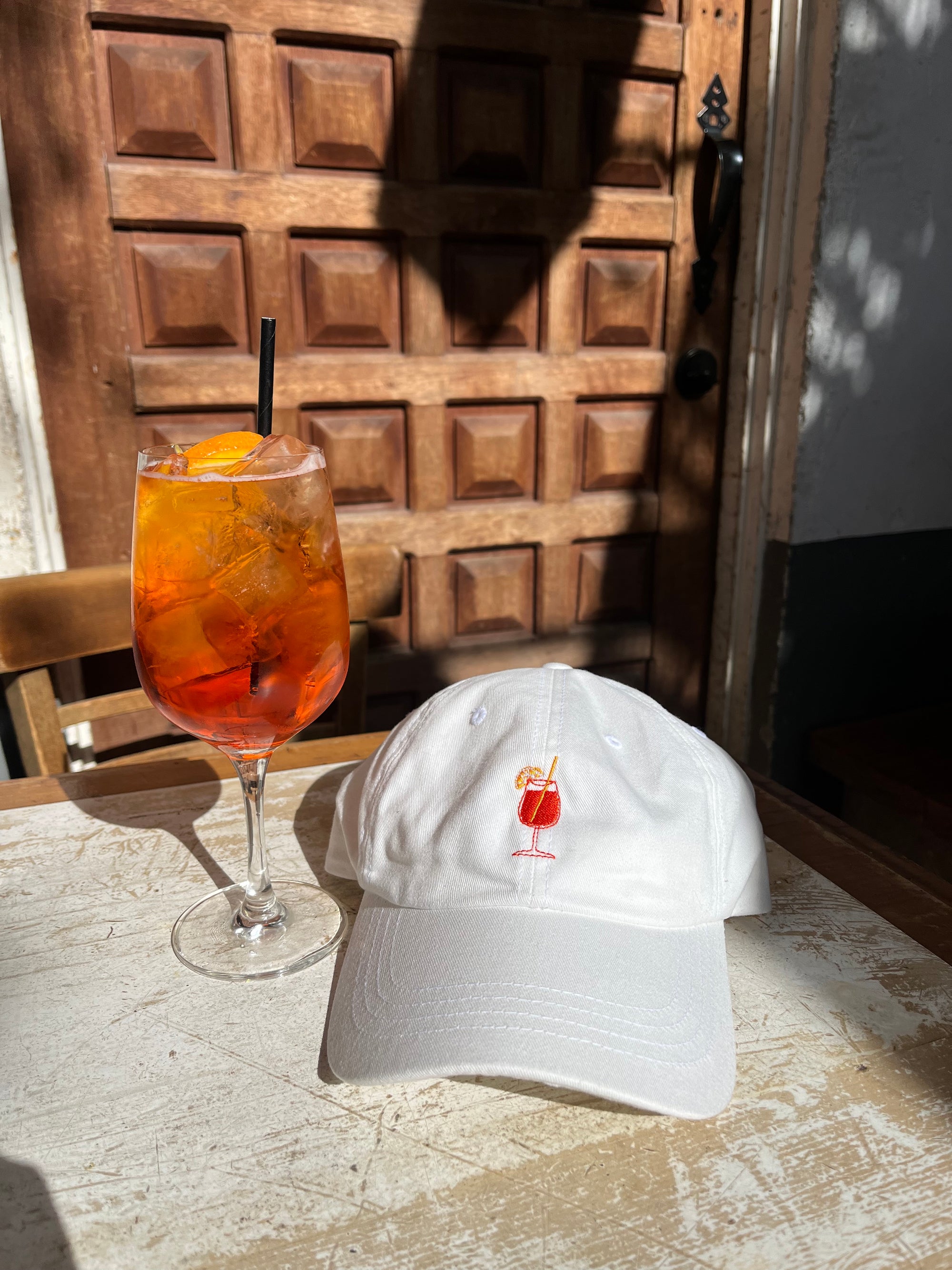 Embroidered Aperol Spritz cocktail design on orange and white dad hat with aperol spritz to the left of it