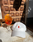 Embroidered Aperol Spritz cocktail design on orange and white dad hat with aperol spritz to the left of it